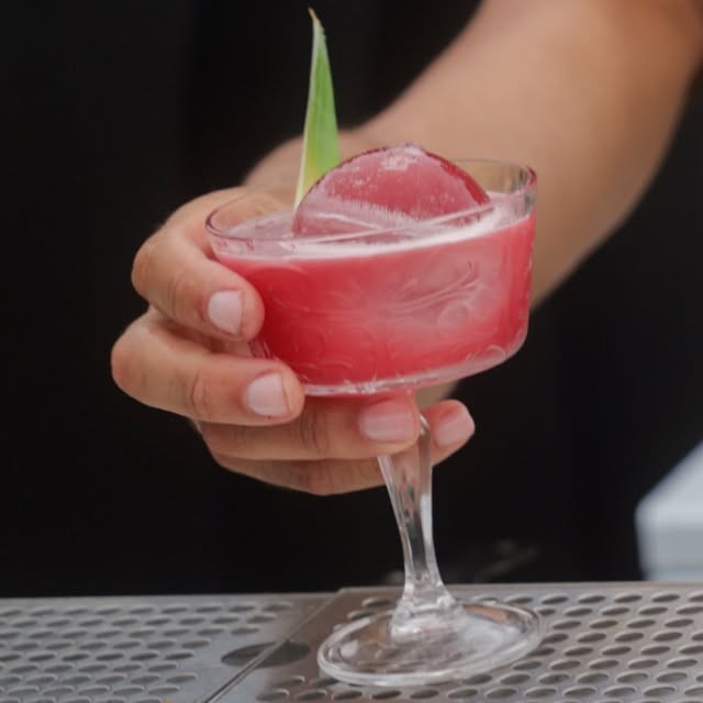 A pink cocktail over a rose-shaped ice sphere