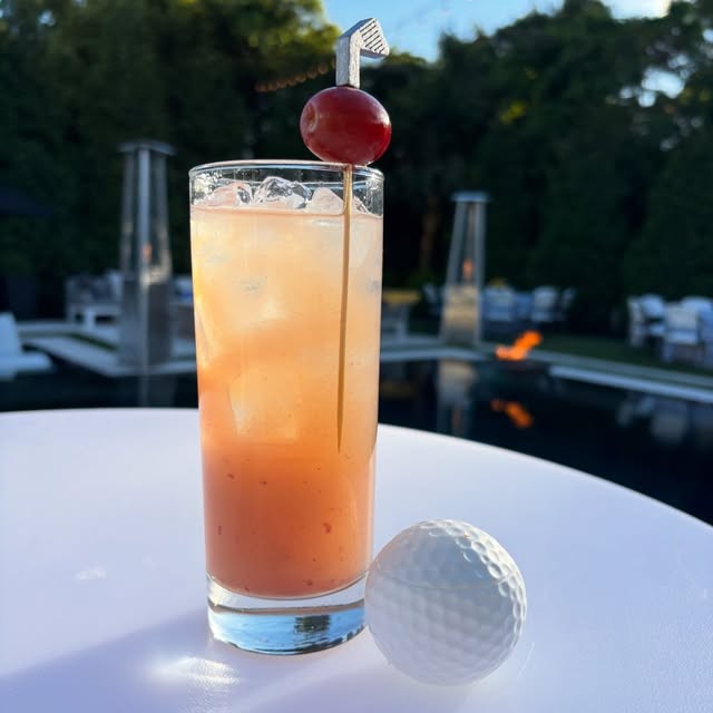 A tall citrus cocktail on a white table at golden hour
