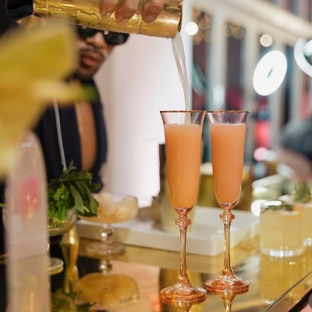Two blush cocktails being poured into gold-stemmed flutes